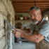 Homme en overalls appliquant du plâtre sur un mur en pierre dans une maison rurale